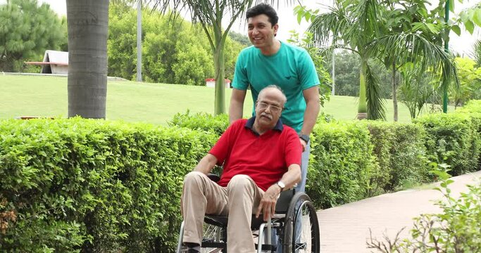 Video of son walking with disabled father in wheelchair at park.
