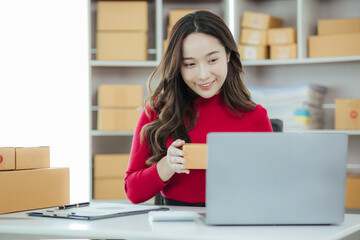 Startup small business entrepreneur or freelance Asian woman using a laptop with box, Young success Asian woman with her hand lift up, online marketing packaging box and delivery, SME concept.