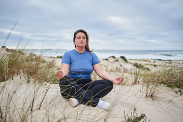 Naklejka na ściany i meble Body positive woman meditating at gloomy beach in the morning