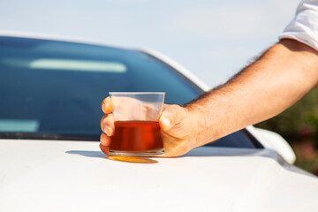 Man's hand holding a glass of whiskey on the background of the car. danger of a drinking alcohol while driving a car and lose a driving license concept