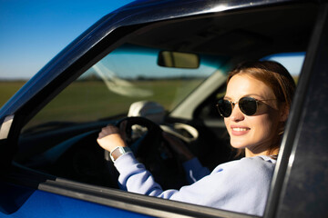 Beautiful young woman driver driving a car on a sunny day smiling.