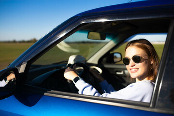 Beautiful young woman driver driving a car on a sunny day smiling.