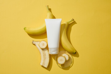 On yellow background, banana cut in slices and a tube without label are arranged. Cosmetic product extracted from Banana (Musaceae) can reduce inflammation in the skin