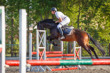 Young sportsman riding horse bounding over obstacle on showjumping competition