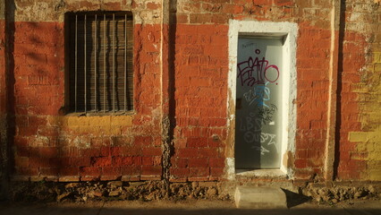 Old abandoned brick building in the street. With closed window and graffiti door