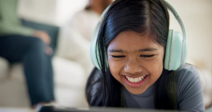 Girl, headphones and tablet for e learning, video call and online education on streaming platform. Young child from Indonesia listening to music, funny games and digital tech or home school on floor
