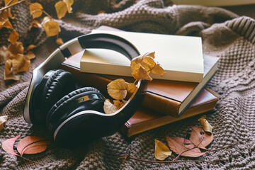 Audiobook or podcast in fall season. Wireless headphones with books and autumn leaves on knitted...