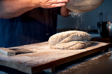 Wooden work surface with flour and fresh bread dough. Man's hand sprinkles flour through a sieve...