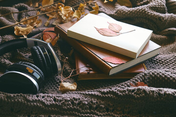 Audiobook or podcast in fall season. Wireless headphones with books and autumn leaves on knitted plaid as concept of learning and education, online courses or music app in cozy fall mood.