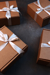 Cardboard boxes on a dark background. Delivery of gifts for the holiday. The cardboard holiday box is tied with a ribbon. Festive packaging.Vertical photo.