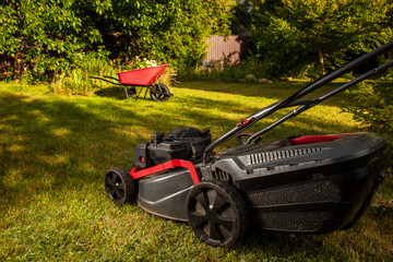 Fototapeta premium Concept of gardening, work, nature. Housework, gardening and country life. Home garden grass cutting woman mowing with lawn mower. Detail of lawn mower. Сutting grass in backyard.