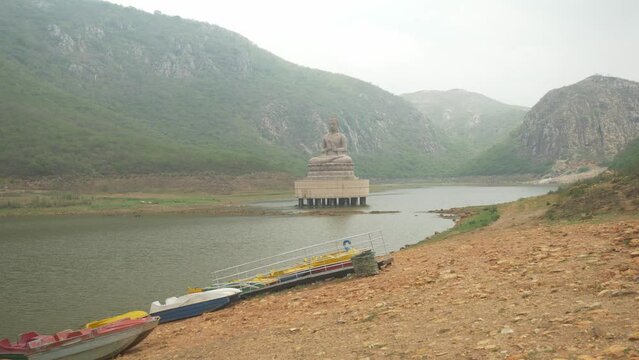 70-foot-high Buddha statue at Ghora Katora lake surrounded by mountains under hazy sky, Rajgir. Bihar