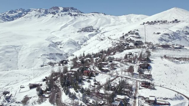 Dolly in aerial view of the houses and the mountain village of Farellones completely snowed in with the exclusive resorts of La Parva and El Colorado, Chile.
