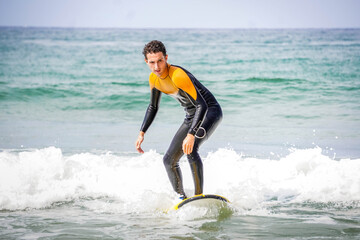 Young Adult Surfer with Wetsuit and Face of Concentration Standing Maintaining Balance on his Board While Ride a Wave 