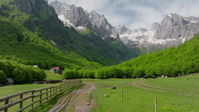 wooden fence and dirt road in mountain valley in spring, countryside village. aerial view fly low over the road. sunny summer day. green landscape around.