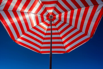 Weiß roter Sonnenschirm vor blauem Himmel als Hintergrund zum Thema Strand, Urlaub und Sonnenschutz