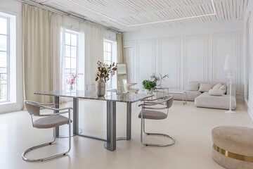 marble dining table and two chairs against the backdrop of a panoramic window into the interior of...