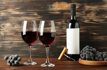 Wine bottle and wine glass with grapes on brown wooden background.