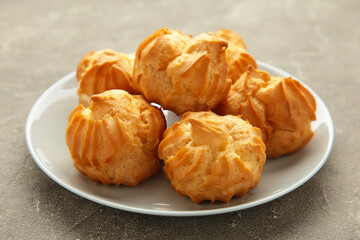 Homemade profiteroles with cream on plate on grey background. Fresh baked golden profiterole.