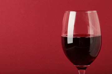 Dark studio shot of glass of red wine on dark red background. Space for text