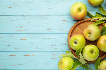 Ripe green apples with green leaves on blue wooden background