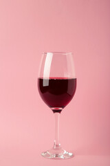 Glass of red wine on pink background. Vertical photo