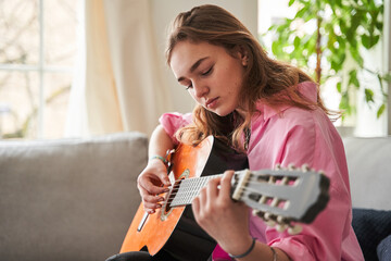 Female musician feeling involved while playing acoustic guitar at home at her room