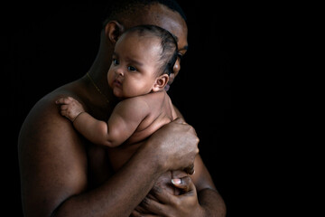 Portrait of shirtless African father holding baby girl on black background