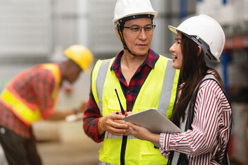 Father or Senior supervisor advises a young worker about warehouse work, both wore safety vest and hardhat for safety