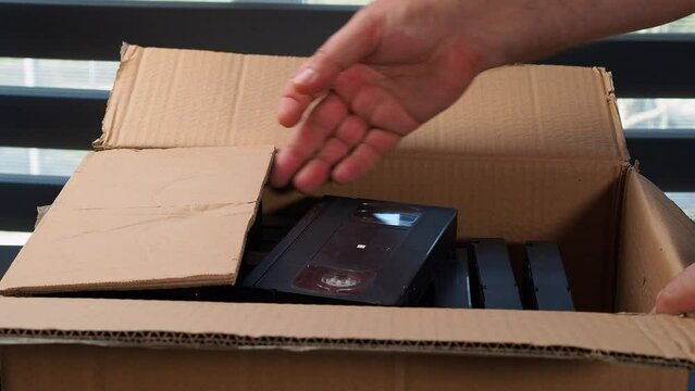 Old VHS tapes in a cardboard box. A man opens a cardboard box with VHS cassettes.