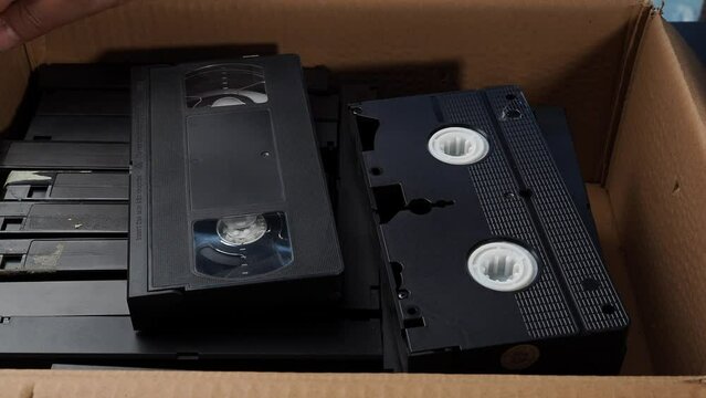 Old VHS tapes in a cardboard box. A man opens a cardboard box with VHS cassettes.