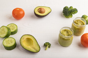 Baby puree with vegetable mix, broccoli, avocado in glass jar on white wooden, side view, copy space