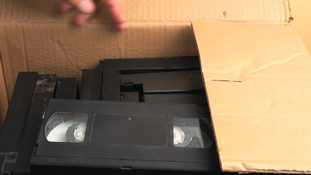 Old VHS tapes in a cardboard box. A man opens a cardboard box with VHS cassettes.