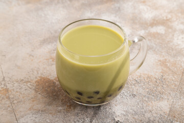 Bubble tea with pistachio and caramel in glass on brown concrete, Side view.