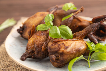 Smoked quails on a ceramic plate on a brown wooden background. Side view