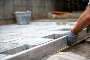 Male hands measuring and leveling sand and cement tiles for precise pavement of the outside patio