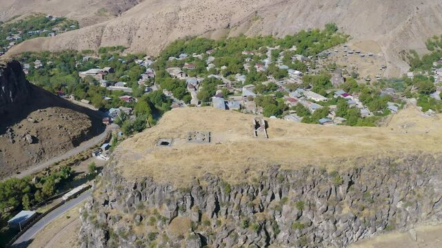 Backward reveal drone footage of Bjni Fortress and village on sunny summer day. Kotayk Province, Armenia.