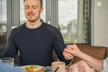 Cropped view of the christian man praying before breakfast and holding hands