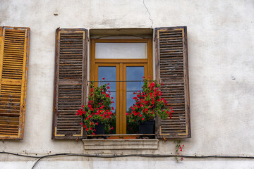 Fototapeta na wymiar Close-up of window with wooden shutters and red flowers on window sill at French City of Toulon on a cloudy late spring day. Photo taken June 9th, 2023, Toulon, France.