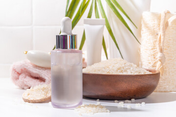 Fototapeta na wymiar Rice Water Serum. Natural organic rice cosmetics. Fermented beauty care, wellness and spa. Transparent white serum drops bottle with rice grain and bath utensils, on white bathroom background