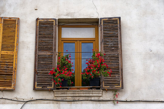 Close-up of window with wooden shutters and red flowers on window sill at French City of Toulon on a cloudy late spring day. Photo taken June 9th, 2023, Toulon, France.
