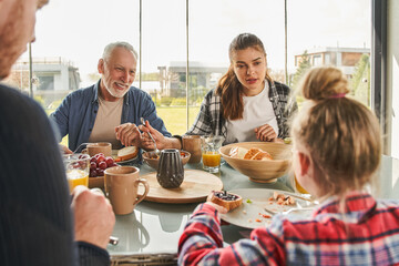 Cheerful three generations positive family having healthy breakfast at home