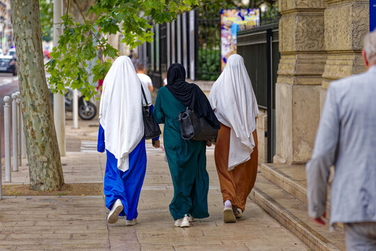 Fototapeta Rear view of three young muslim women at French City of Toulon on a cloudy late spring day . Photo taken June 9th, 2023, Toulon, France.