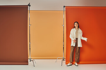 stylish asian model in autumn outfit standing on multicolored backdrop, leather pants and outerwear