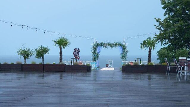 White Wooden Arch and Wedding chairs for outside ceremony with marriage decoration under cold rain during adverse weather conditions. Bad weather, heavy rain, ruined wedding. Setting stage festive