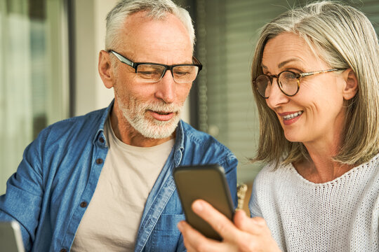 Smiling senior woman holding smartphone and showing it to old ma