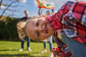 Overjoyed little kid looking camera while playing with her parents outdoors