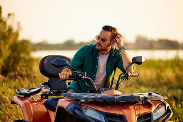 Fototapeta na wymiar An adult man with sunglasses on, sitting on a quad bike and looking around.