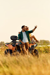 A smiling love couple taking a selfie photo with the phone on a quad bike in nature. © bnenin