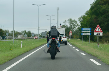 Back rear view of biker driving on asphalt road in a rural area with blurred traffic signs and vehicles